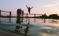 A person jumps into a lake from a dock at sunset, with friends watching from the dock.