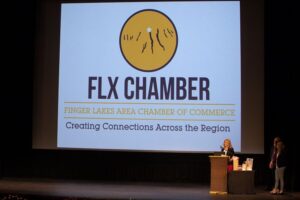 A speaker presents at a Finger Lakes Area Chamber of Commerce event, with the FLX Chamber logo on a large screen.
