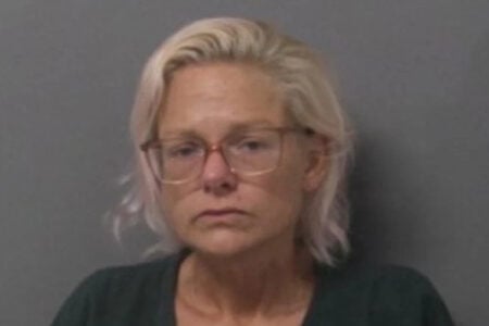Mugshot of a blonde woman with glasses and a neutral expression against a gray background.