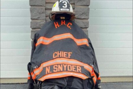 Firefighter Chief N. Snyder's jacket and helmet, number 3, hang against a building with a garage door.