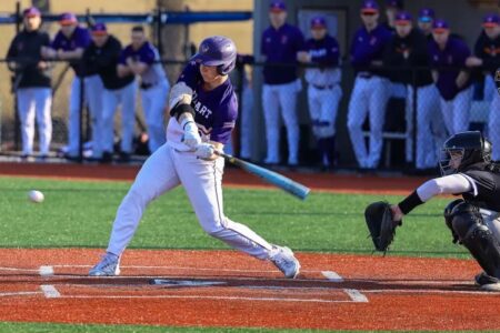 A Hobart College baseball player in a purple jersey swings a bat, hitting a baseball during a game.