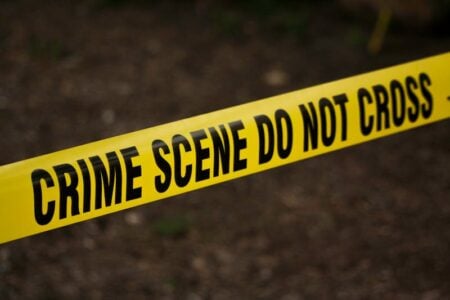 Yellow 'CRIME SCENE DO NOT CROSS' tape stretches across a blurred outdoor background.