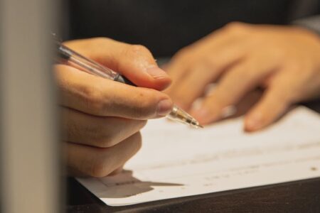 Close-up of a person's hands holding a clear pen and writing on a white document.