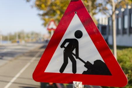 A red and white triangular road sign with a black figure shoveling, indicating road work ahead.