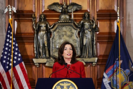 Governor Kathy Hochul speaks at a podium with US and New York flags, and the NY State Seal behind her.