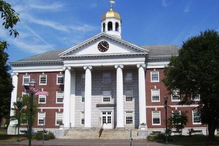 Auburn City Hall, a brick and stone building with white columns, a clock, and a golden dome, under a blue sky.