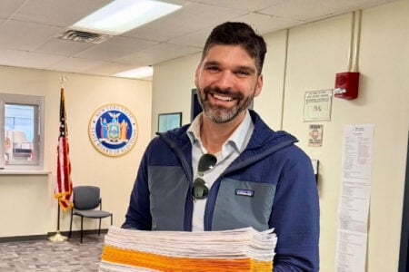 Smiling man Aaron Gies holds a stack of petitions inside the NY State Board of Elections office.