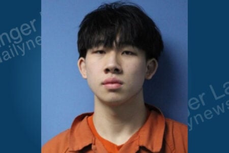 Mugshot of a young man with dark hair wearing an orange jumpsuit against a blue background.
