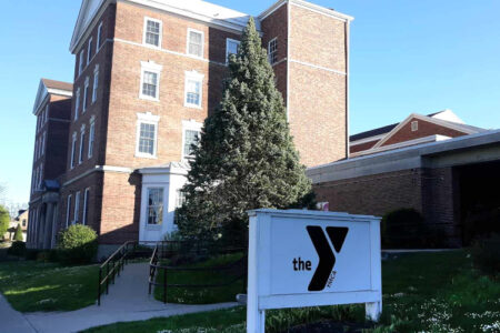 The Auburn YMCA building, a multi-story brick structure, is viewed from the street on a sunny day with its sign.