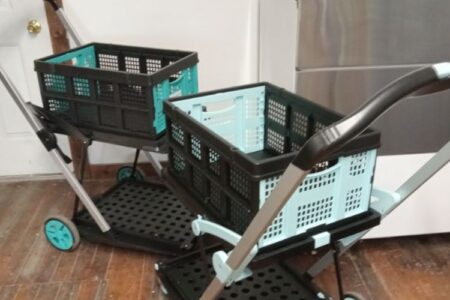 Two folding utility carts with teal and black crates on a wood floor, next to a stainless steel appliance.