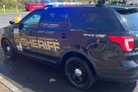 A black Cayuga County Sheriff's SUV with gold lettering and emergency lights on, being washed outdoors.