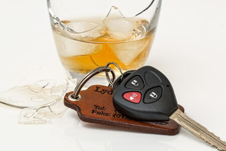 Car keys lie next to a broken glass containing a drink with ice, and glass shards, symbolizing impaired driving.