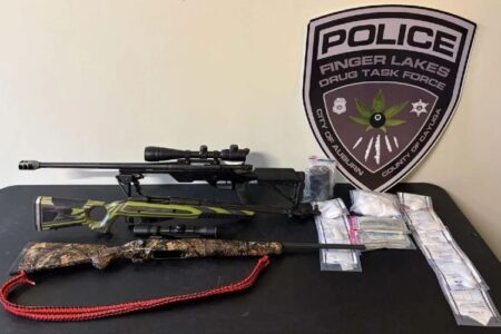 Three rifles, bags of drugs, and a Finger Lakes Drug Task Force patch are displayed on a table.