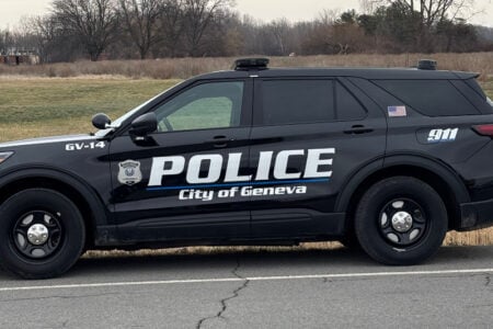 A black Geneva Police Department SUV parked on the side of a road with trees in the background.
