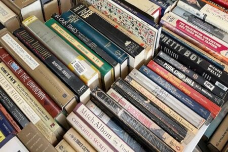Stacks of used books, including history and literature titles, are displayed at a local book sale.