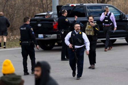 Law enforcement officers, some armed, gather near a black pickup truck at a scene related to a Michigan synagogue attack.