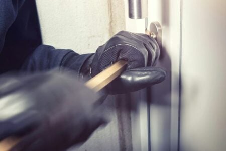 Gloved hands use a crowbar to pry open a door handle during a break-in.