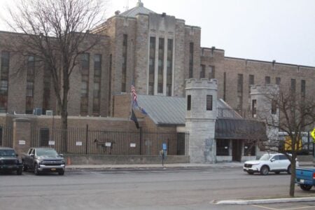 Exterior view of Auburn Correctional Facility, a large brick building with turrets, and vehicles in the foreground.