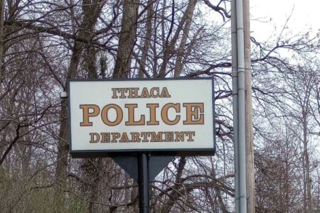 The Ithaca Police Department sign stands outdoors against a backdrop of bare trees.