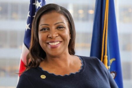 New York Attorney General Letitia James smiles in front of the US flag and New York State flag.