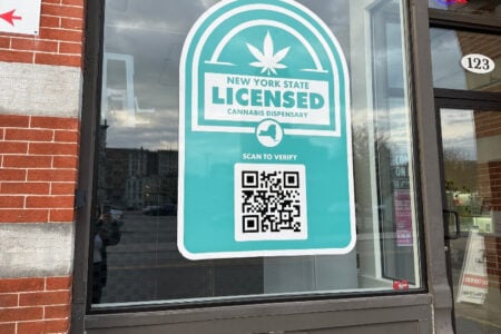 A teal and white decal on a window reads 'New York State Licensed Cannabis Dispensary' with a cannabis leaf and QR code.