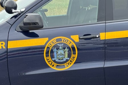 Close-up of a New York State Police vehicle door showing the official seal and yellow stripe.