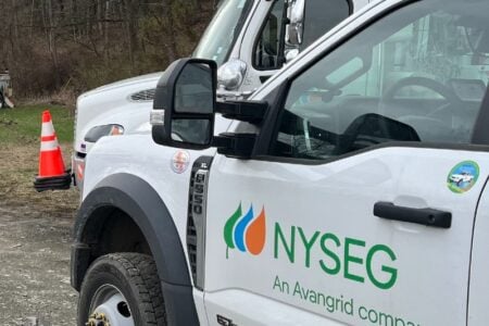 A white NYSEG utility truck is parked outdoors with an orange safety cone nearby.