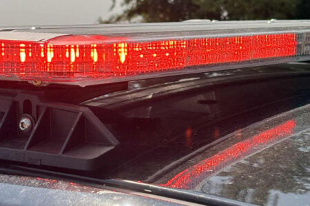 Flashing red emergency lights on top of a police vehicle, reflecting on its dusty roof.
