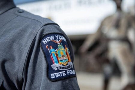 Close-up of a New York State Police officer's grey uniform sleeve with the "Excelsior" patch.