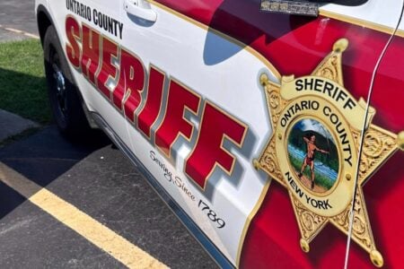 Side view of an Ontario County Sheriff's vehicle, white and red, with badge and 'Serving Since 1789'.