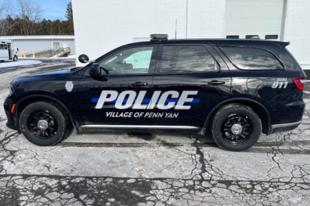 A black Village of Penn Yan police SUV is parked on a snowy surface outside a white building.