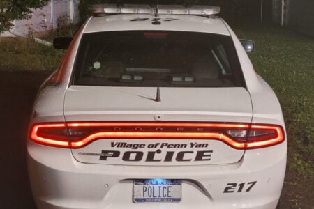 Rear view of a white Village of Penn Yan Police Dodge Charger at night, with illuminated taillights.