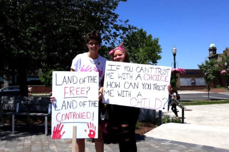 Two protestors hold signs about reproductive rights on a sunny day in downtown Geneva.