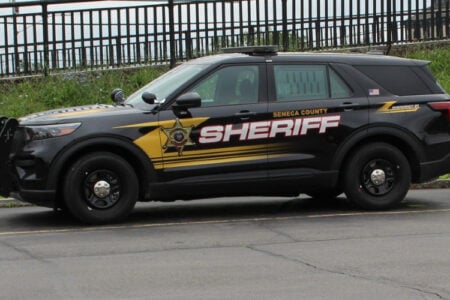 A black Seneca County Sheriff's SUV is parked on asphalt next to a black metal fence.