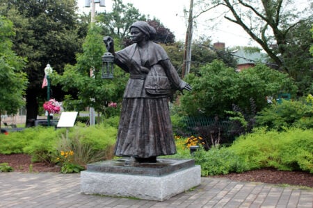 Bronze statue of Harriet Tubman holding a lantern in a landscaped park in Auburn, NY.