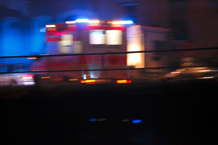 Ambulance with flashing red and blue lights speeds by at night, motion blurred.