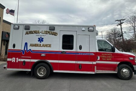 New Aurora-Ledyard Fire District ambulance A1, red and white, parked outside a station under a cloudy sky.