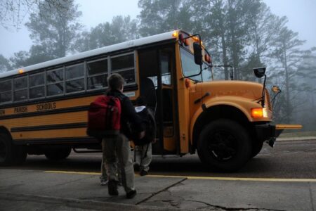 Students board a yellow school bus on a foggy morning.