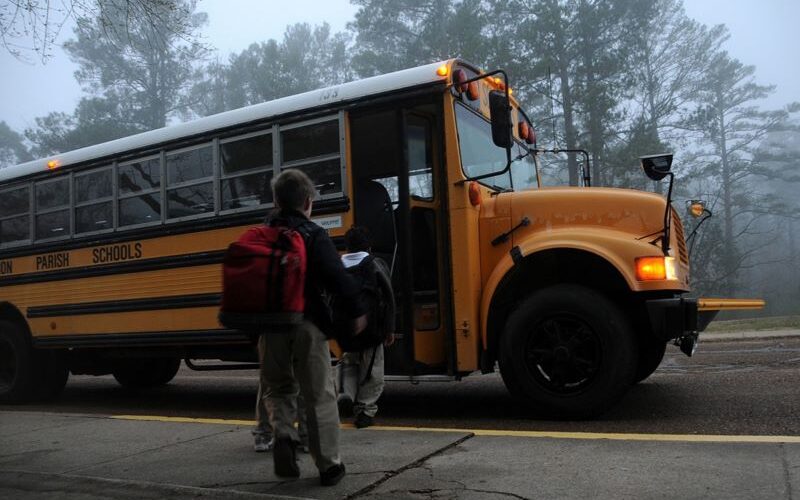 Students board a yellow school bus on a foggy morning.