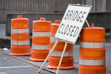 A 'Bridge Closed' sign stands among orange traffic barrels on a road.