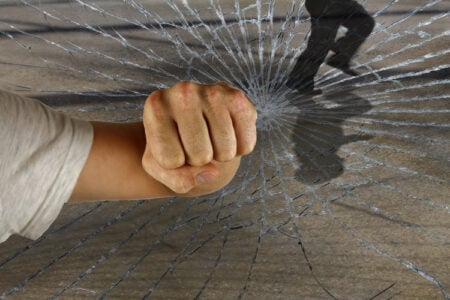 A clenched fist punches through cracked glass, with a blurry shadow of a person running in the background.