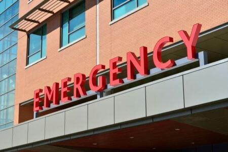 Exterior of a hospital emergency room with the word "EMERGENCY" in red letters above the entrance.