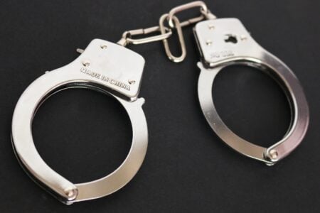 Shiny metal handcuffs are shown on a dark background.