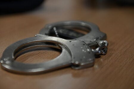 Metal handcuffs lie on a wooden surface.