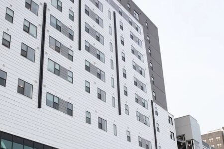 Exterior view of a modern high-rise apartment building with white siding and dark accents, seen from below.
