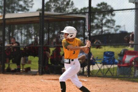 A softball player in a yellow and green uniform with a white helmet bats during a game.