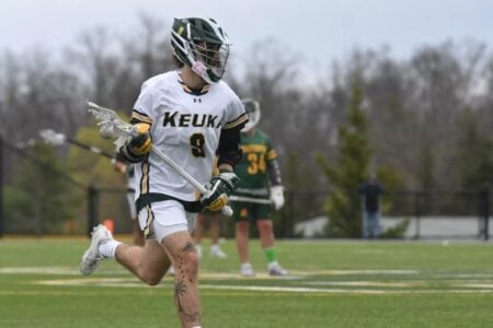 Keuka College lacrosse player #9 runs with his stick on a grass field during a game.