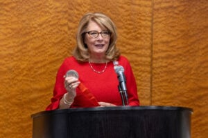Senator Pam Helming in a red dress holds a silver medal at a podium.