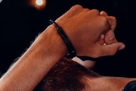 Close-up of a person's clasped hands, one wrist wearing a black handcuff, over reddish-brown hair.