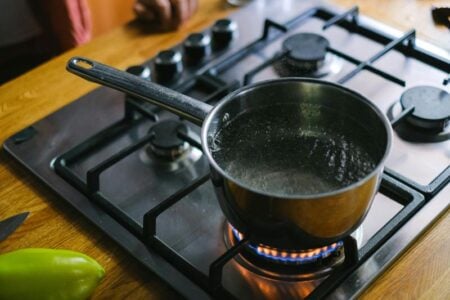 A pot of water boils on a gas stovetop in a kitchen setting with a wooden counter.